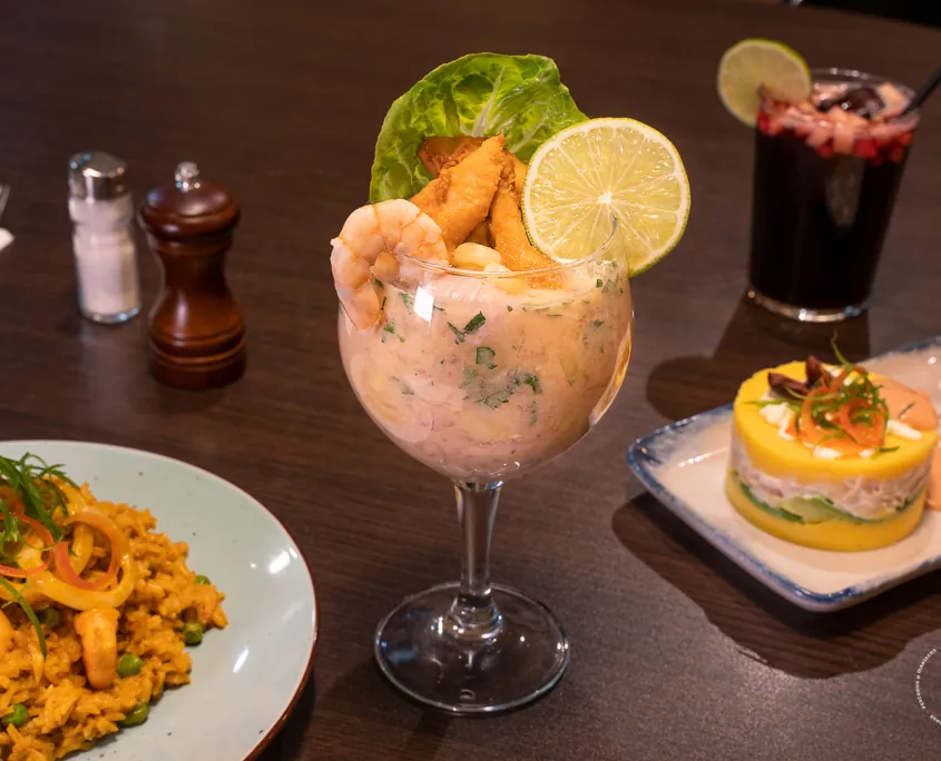 Mesa con leche de tigre en copa, arroz con mariscos y una causa